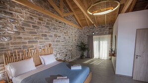 A bedroom with a stone wall, wooden beams, a bed with blue bedding, and a hanging light fixture.
