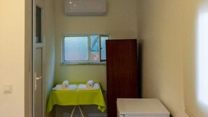 A compact room with a bed, a small table with towels, a white refrigerator, and a window with blinds. - Korfez Pansiyon (Ayvalik)