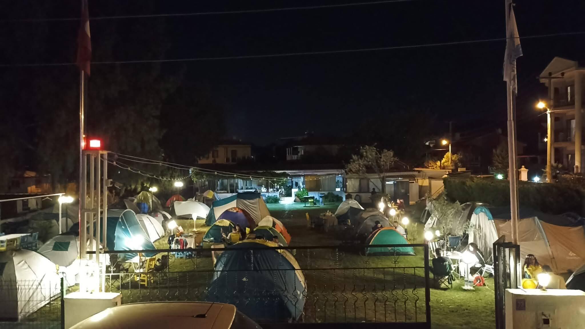 A nighttime view of a campsite with multiple tents and a building in the background.