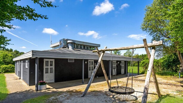 A two-story building with a covered porch and a swing set in the yard. - 4 Person Holiday Home in Hampen (Hampen)
