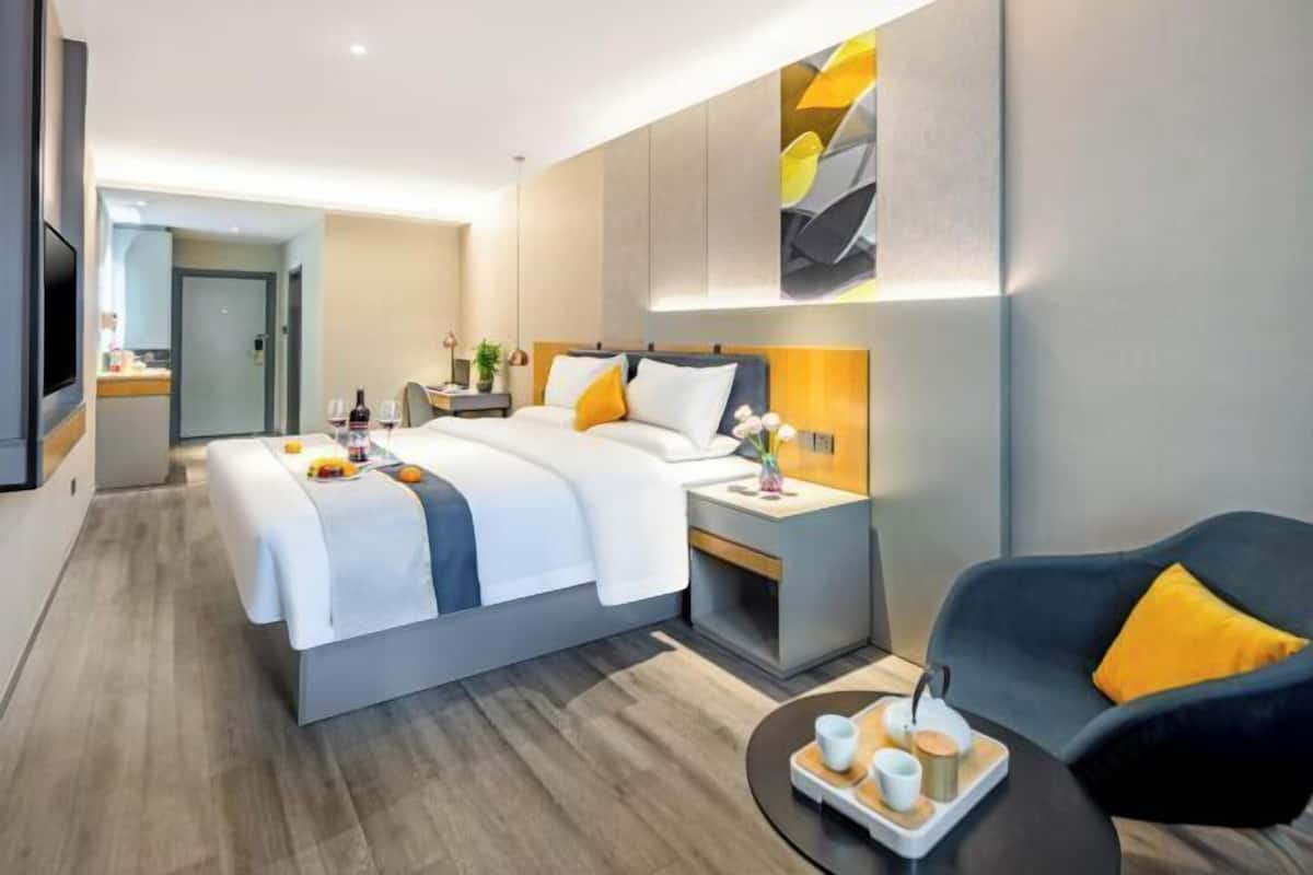 A modern hotel room with a large bed, bedside tables, a sofa, and a small dining table with a tray of breakfast items.