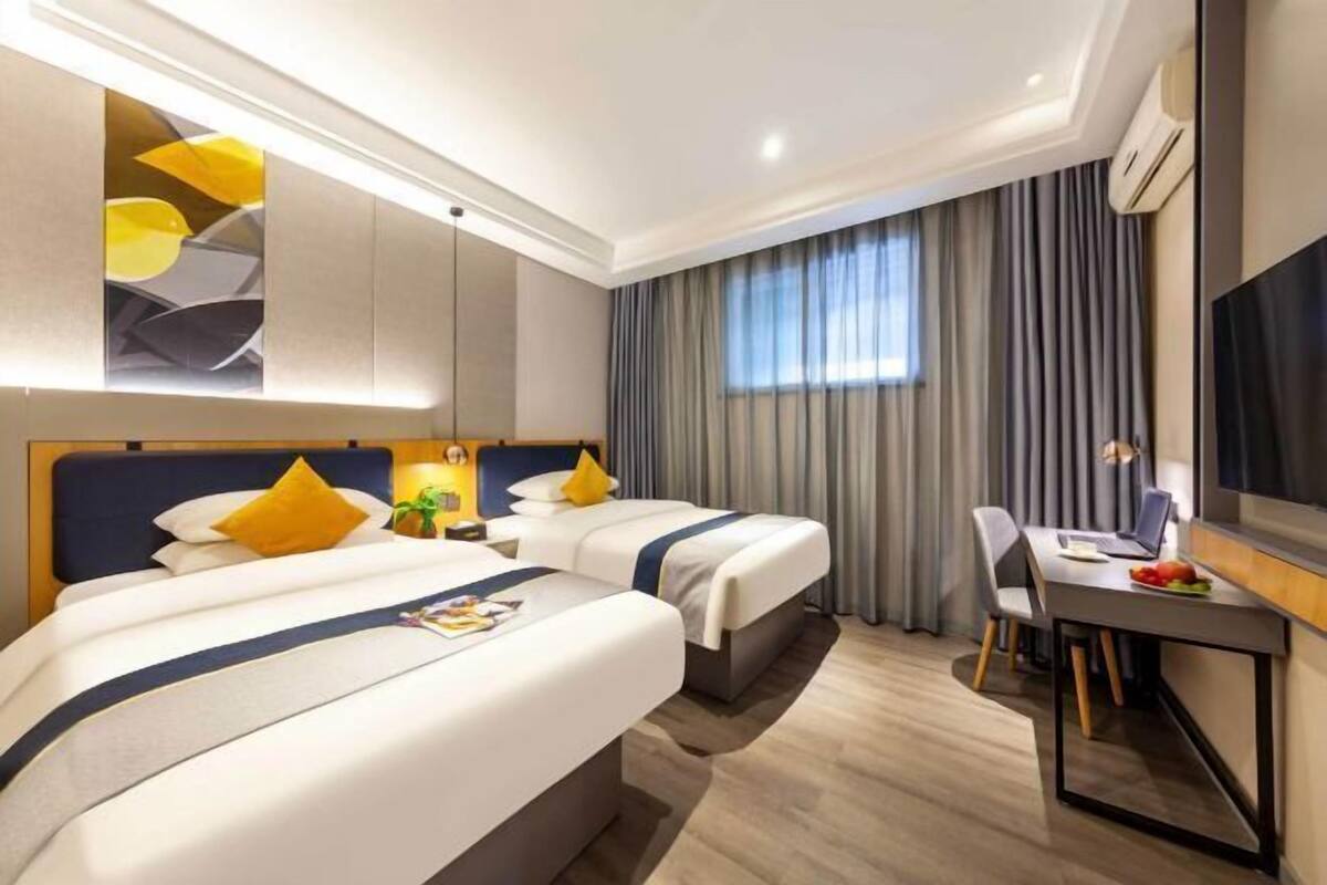 A hotel room with two beds, a desk, a chair, a TV, and a large window with curtains.