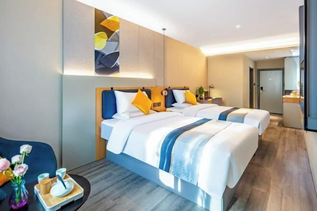 A hotel room with two beds, a small table with a vase of flowers, and a modern light fixture.