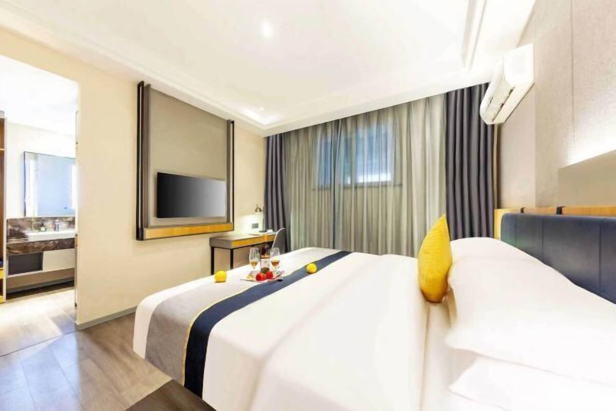 A hotel room with a bed, a desk, a flat-screen TV, and a window with curtains.