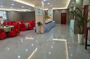A hotel lobby with rows of red chairs, a reception desk, and a plant.
