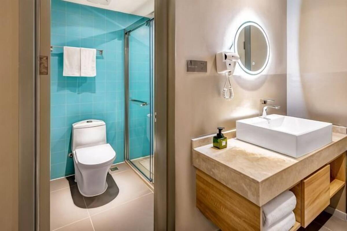 A modern bathroom with a glass shower enclosure, a white toilet, and a beige vanity with a sink and mirror.