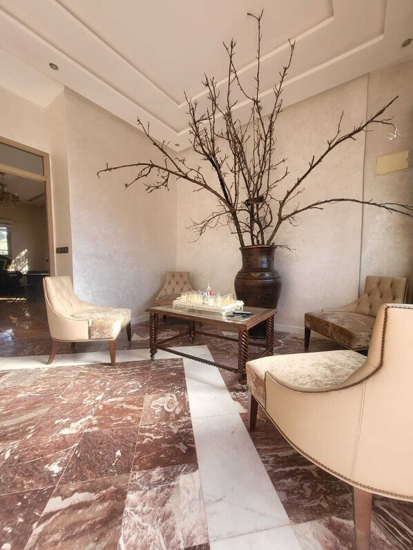 A spacious lobby with marble flooring, a large vase with branches, and two leather armchairs.