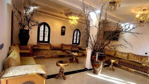 A spacious lounge area with a high ceiling, ornate chandeliers, and a central seating arrangement.