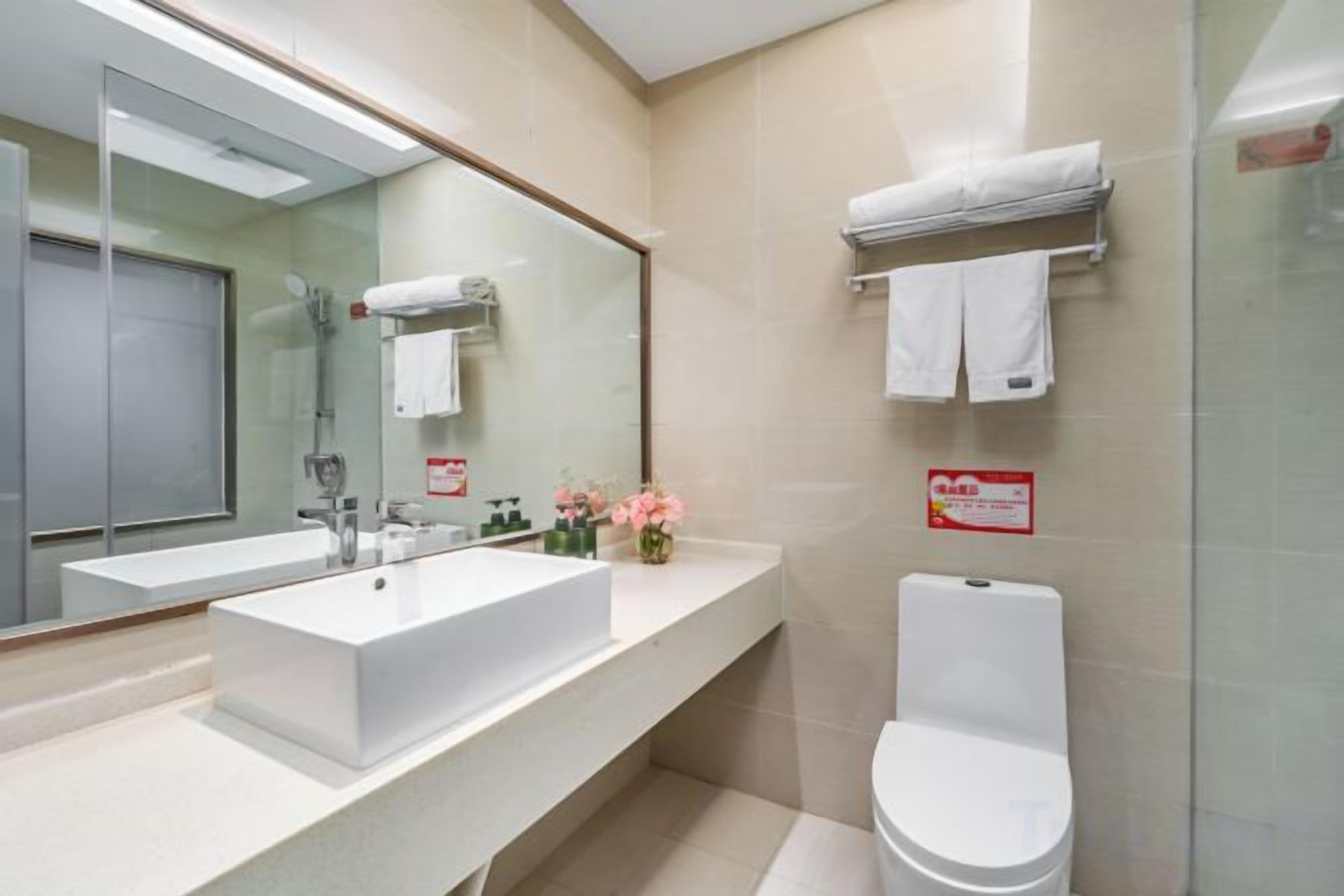 A modern bathroom with a large mirror, a white sink, and a toilet.