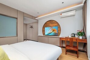 Une chambre d’hôtel équipée d’un lit, d’un bureau, d’une chaise, d’un téléviseur fixé au mur (qui est en bois) et d’un appareil de climatisation.