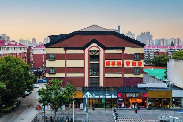 Un edificio de varios pisos con una entrada central, rodeado de tiendas más pequeñas en la planta baja.