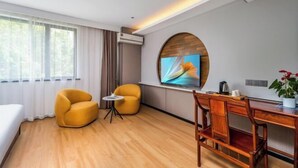 A hotel room with a bed, two yellow armchairs, a small table, a wooden desk, a TV mounted on a wall, and a potted plant. - Yiting Four Seasons Hotel (Shanghai Lujiazui Pudian Road Subway Station) (Shanghai)