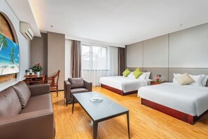Una camera d'albergo con due letti, un divano, un tavolo da pranzo e un quadro raffigurante una spiaggia.