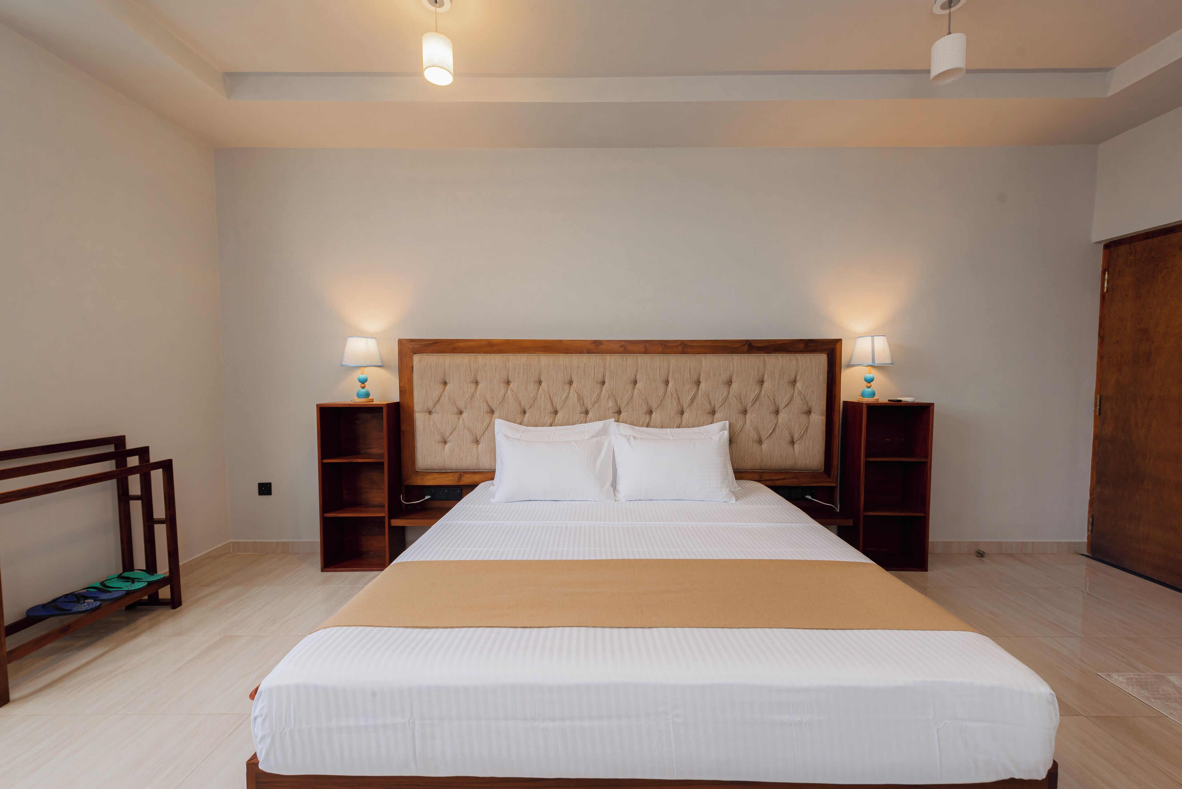 A large bed with a wooden headboard, two bedside tables with lamps, and a wooden bench against the wall.