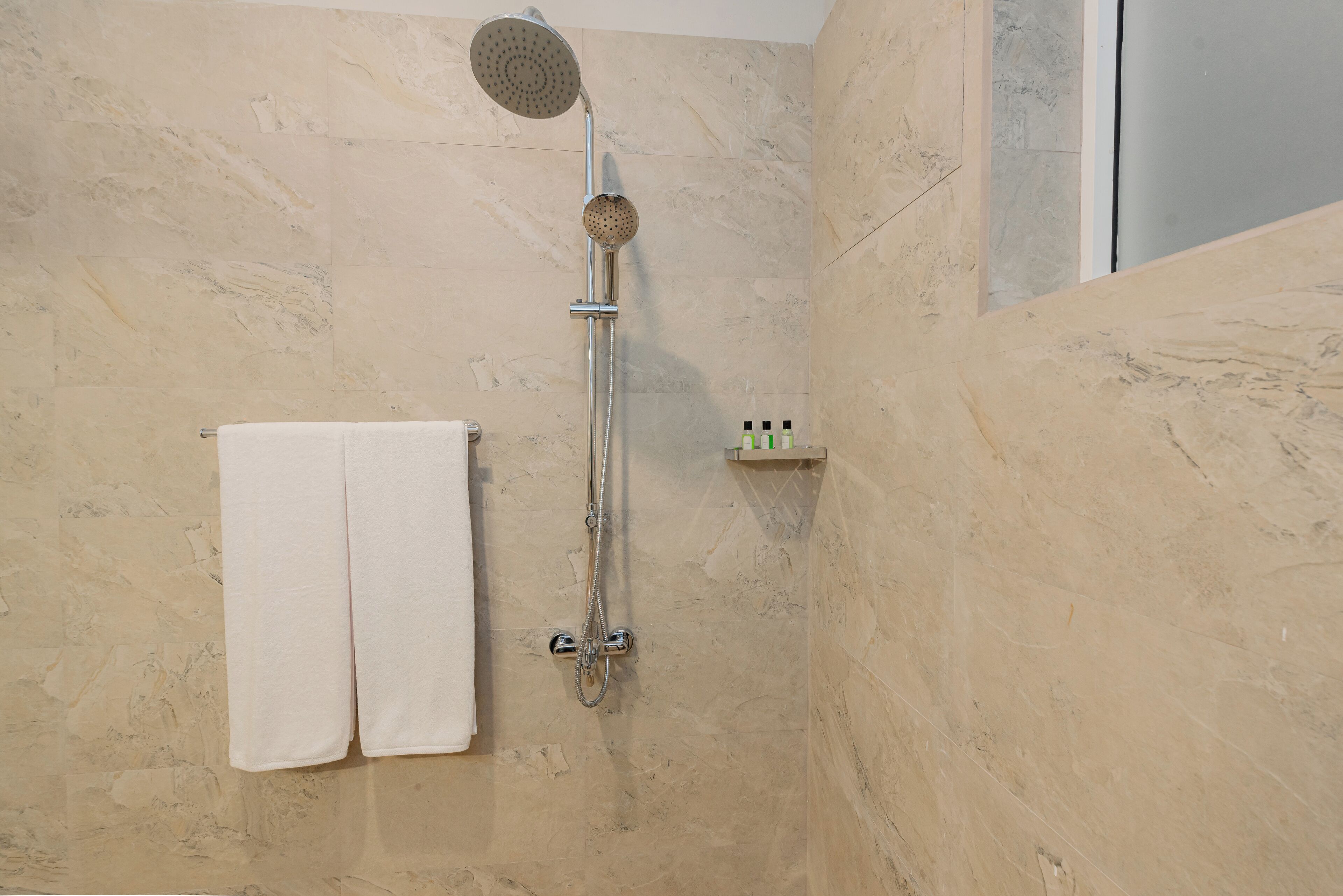 Un baño con ducha, un perchero con una toalla blanca y un estante pequeño con artículos de aseo.