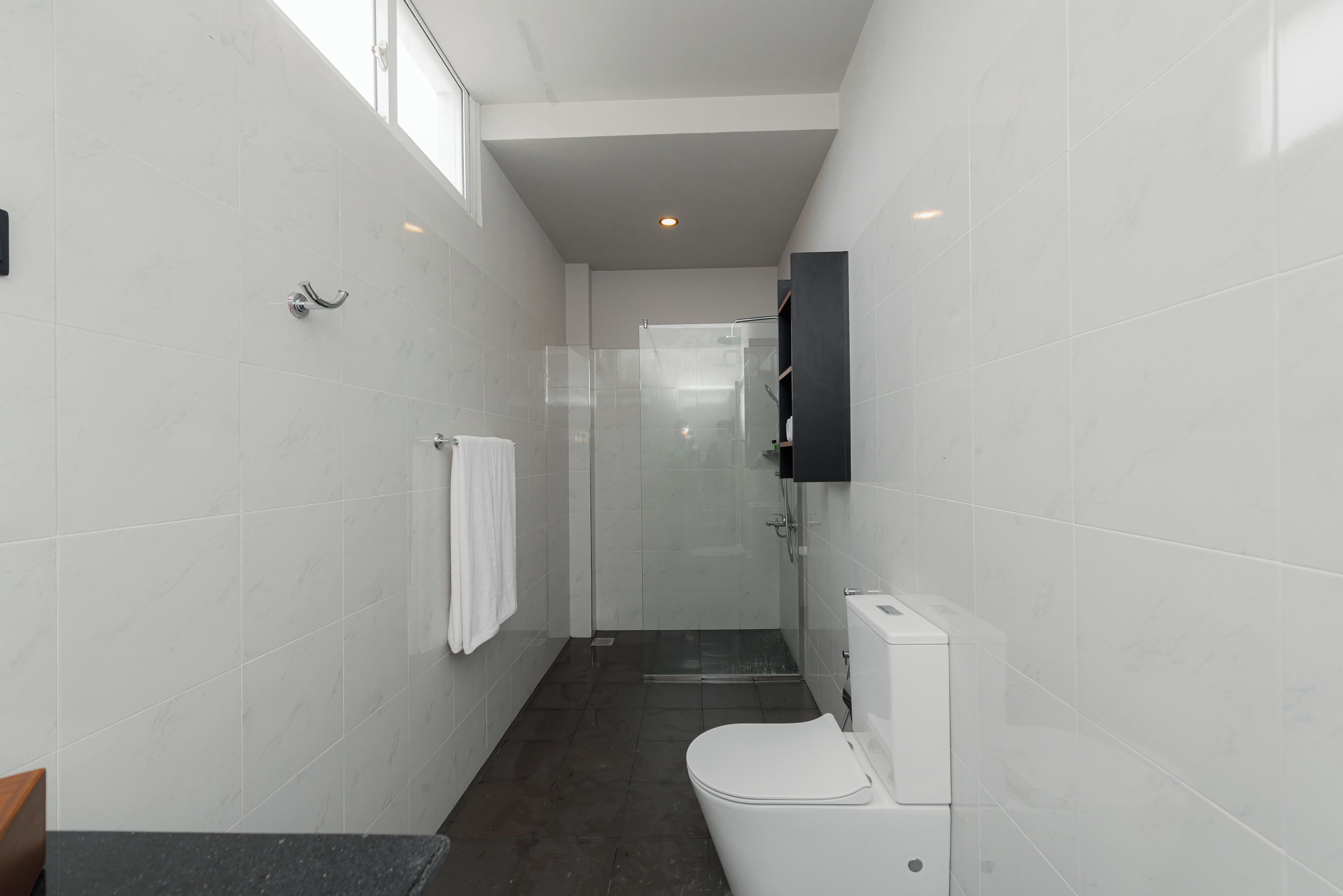 Un baño moderno con azulejos blancos, cabina de ducha de vidrio, inodoro y un armario de medicinas negro.