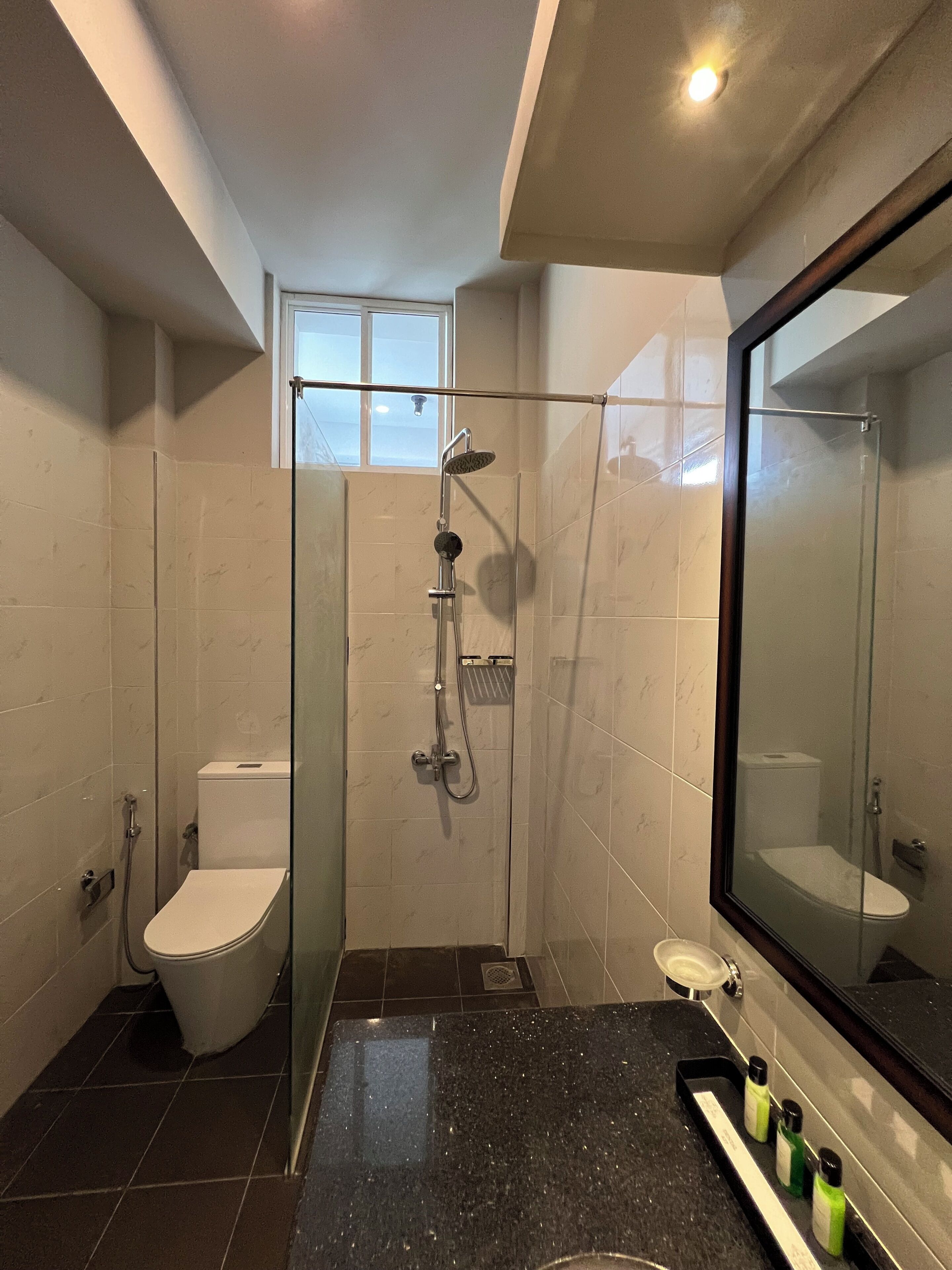 Un baño moderno con ducha de vidrio, inodoro y lavamanos con artículos de aseo.