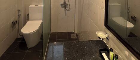 Un baño moderno con ducha de vidrio, inodoro y lavamanos con artículos de aseo.