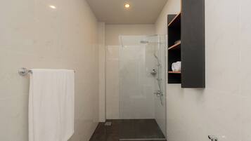A modern bathroom with a glass-enclosed shower, a white towel hanging on a rack, and a dark wooden shelf with toiletries.