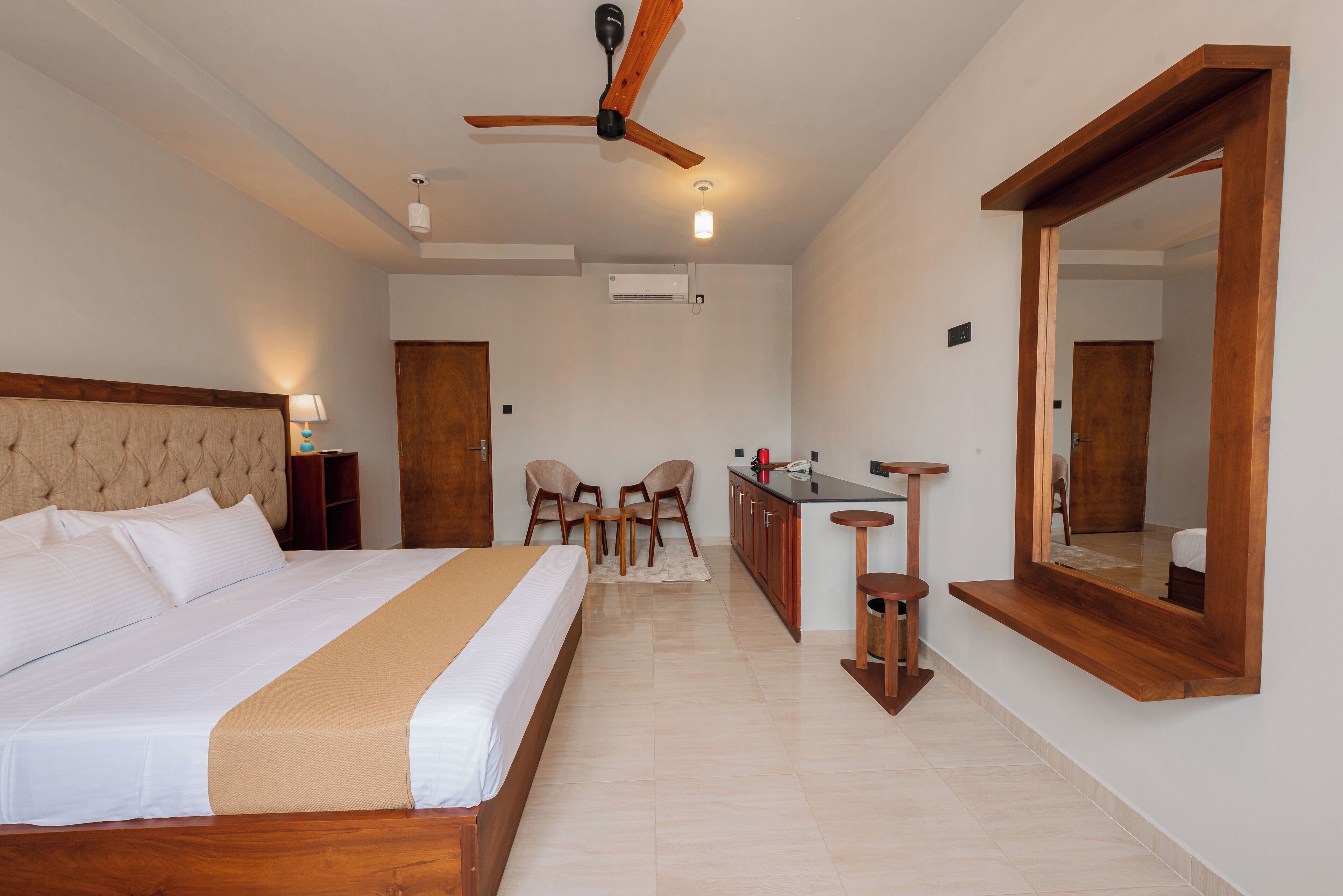 A hotel room with a large bed, a desk with a chair, a mirror, and a ceiling fan.