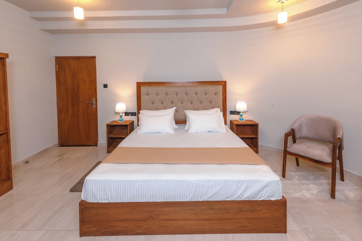 Un dormitorio ordenado con una cama grande, dos mesitas de noche con lámparas, un armario de madera y una silla.