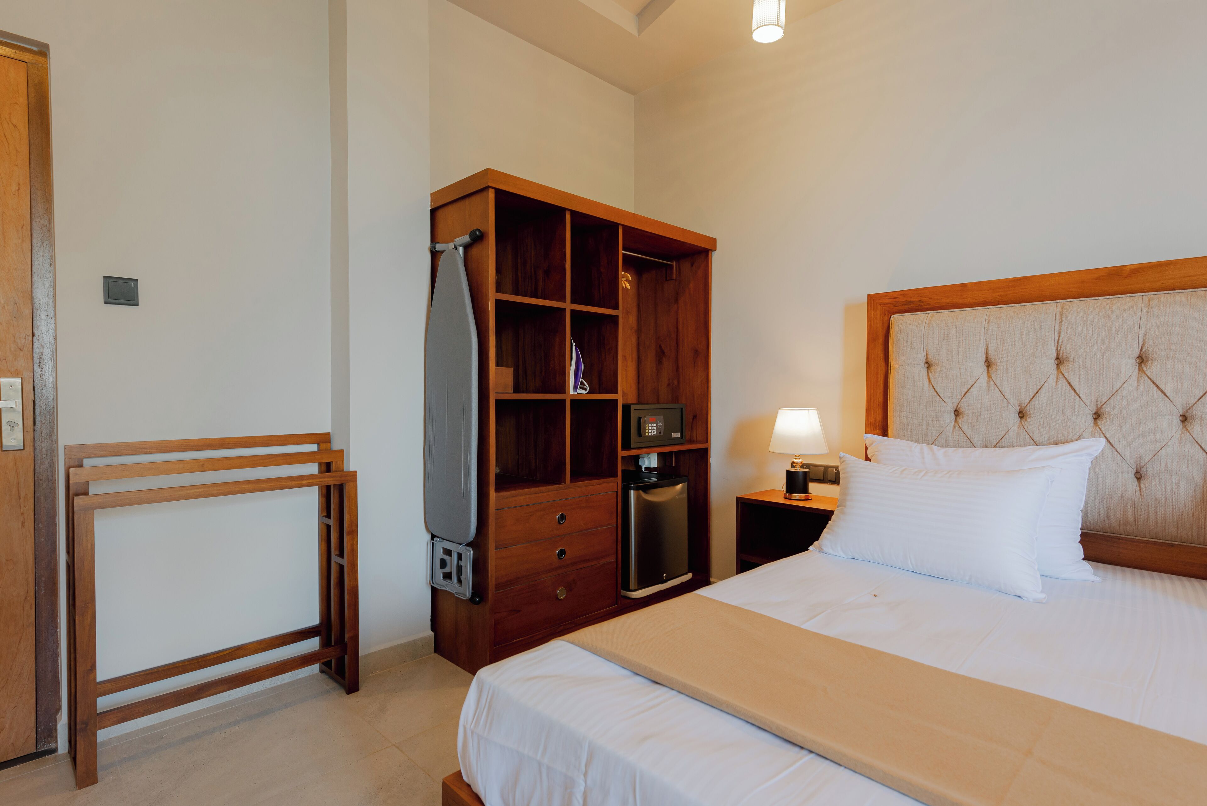 Habitación de hotel con una cama, un armario de madera, un microondas y una mesita de noche con lámpara.