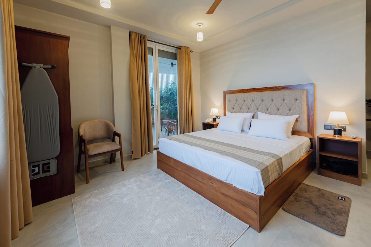 Un dormitorio con una cama grande, una silla, un escritorio y un ventanal corredero que da a un balcón.