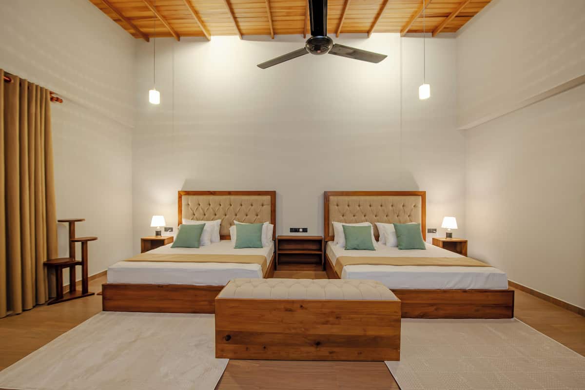 Habitación de hotel con dos camas, techo de madera y un banco central.
