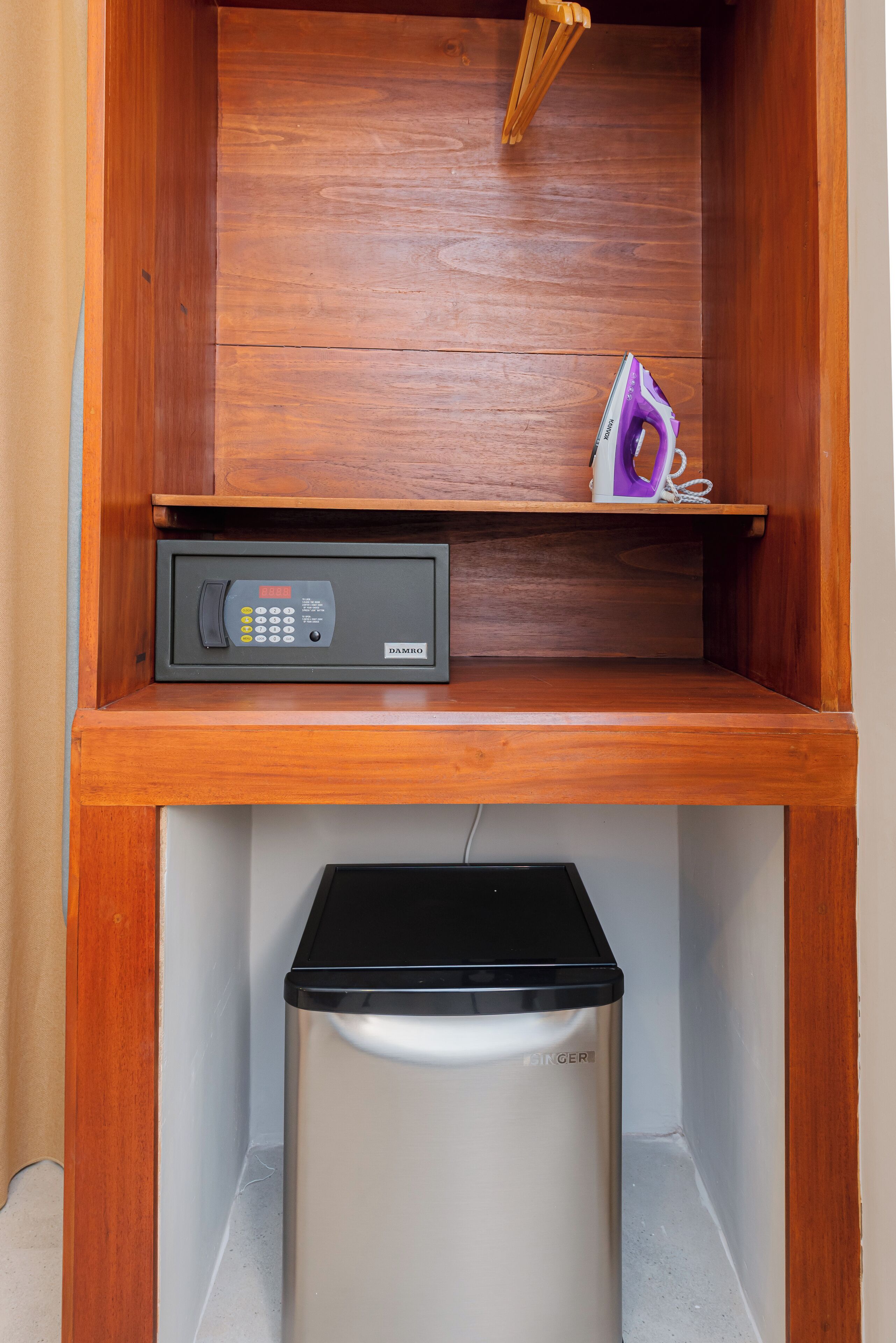 Une petite pièce comprenant un meuble en bois, une petite étagère, un four à micro-ondes et une poubelle.