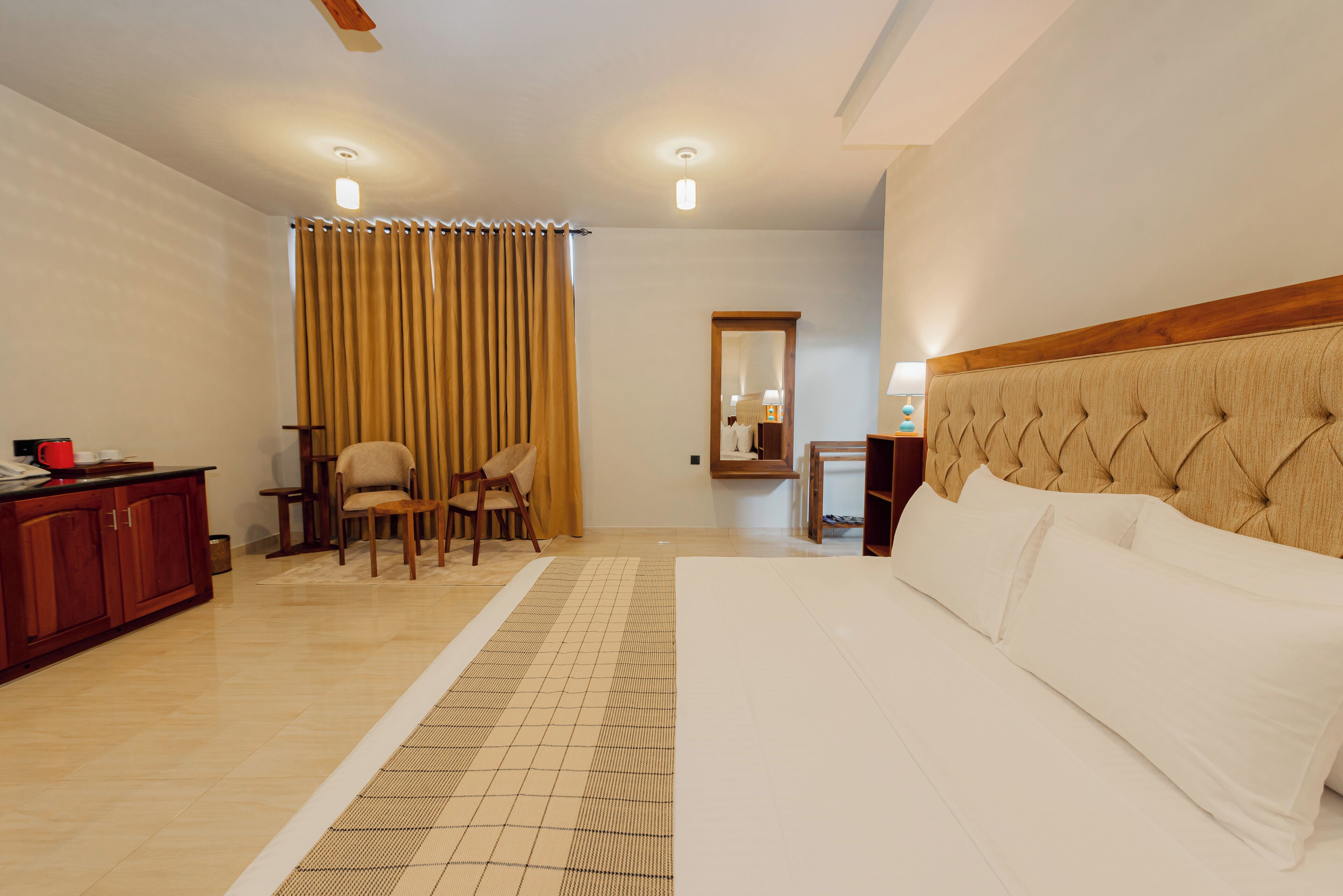 Habitación de hotel con una cama grande, cabecero de madera, escritorio con silla, espejo y ventana con cortinas.