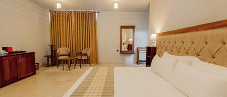 Habitación de hotel con una cama grande, cabecero de madera, escritorio con silla, espejo y ventana con cortinas.