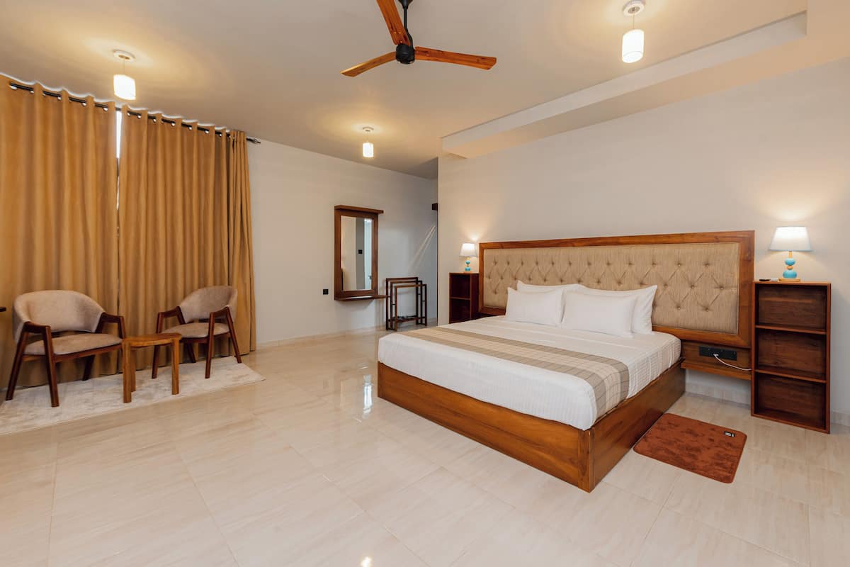 Un dormitorio amplio con una cama grande, dos sillones, un ventilador de techo y una mesita de noche con lámpara.