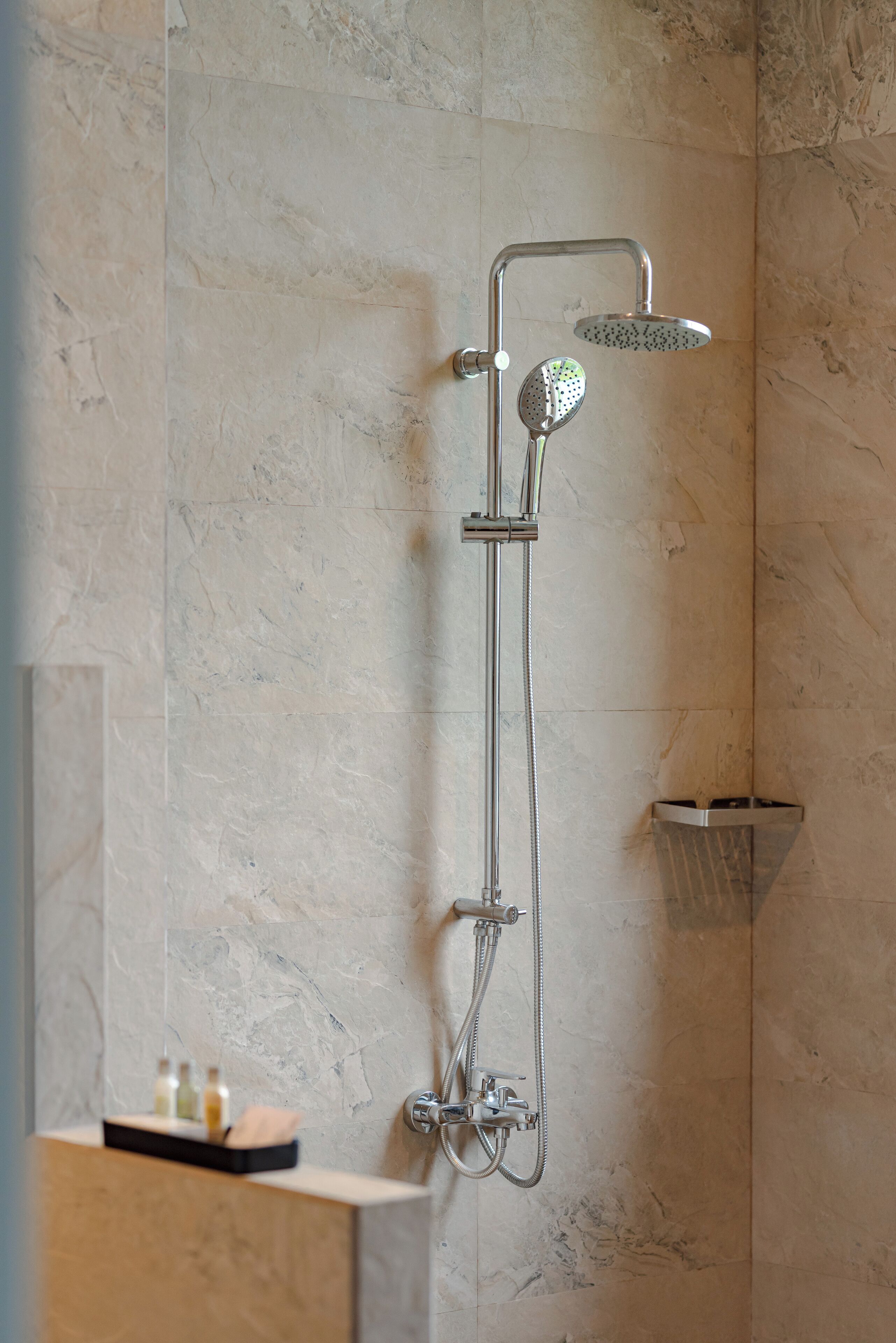 A modern bathroom with a vertical shower unit, marble walls, and a small shelf with toiletries.