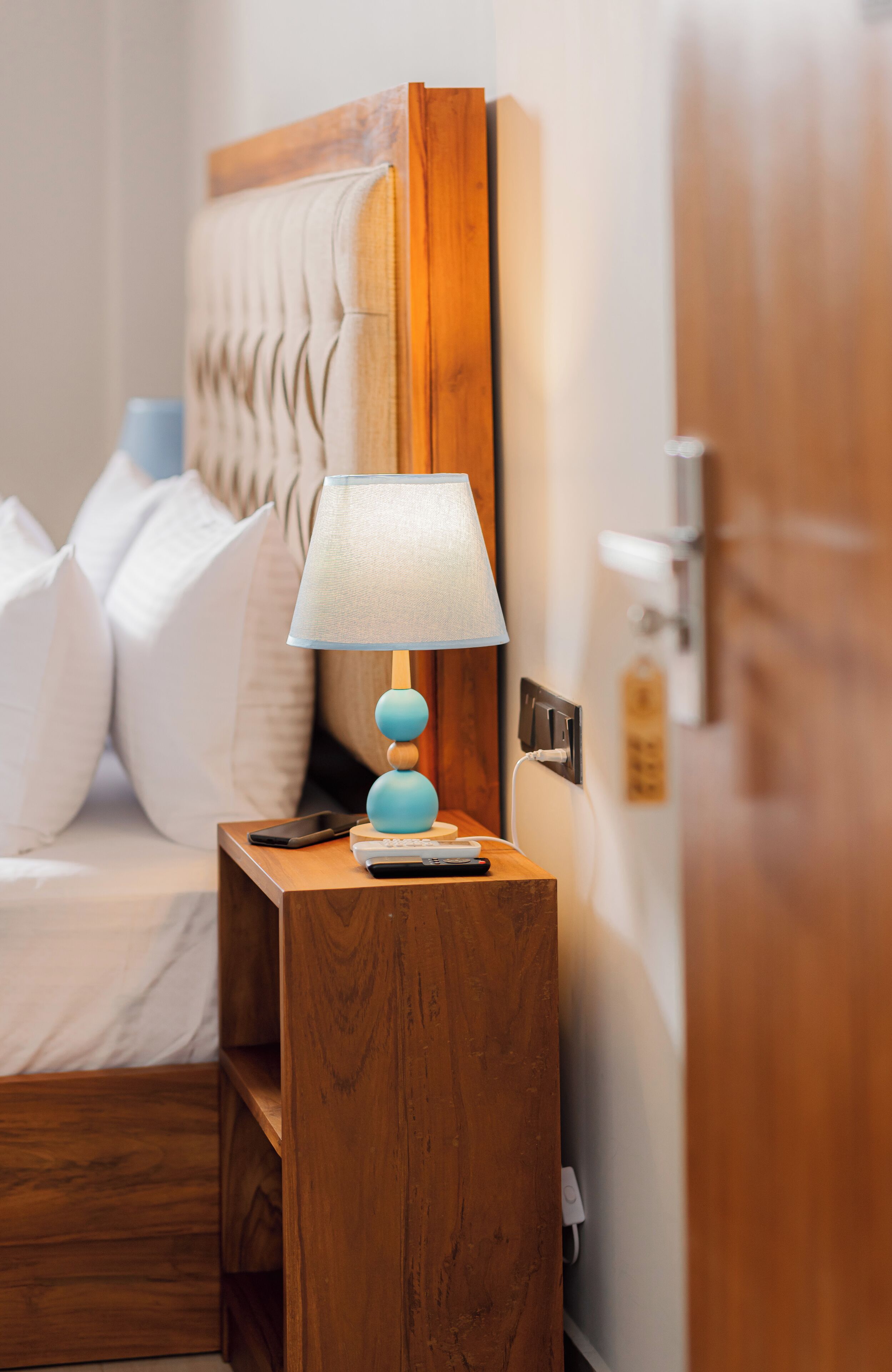 A neatly made bed with white linens, a wooden nightstand with a blue lamp, and a wooden headboard.