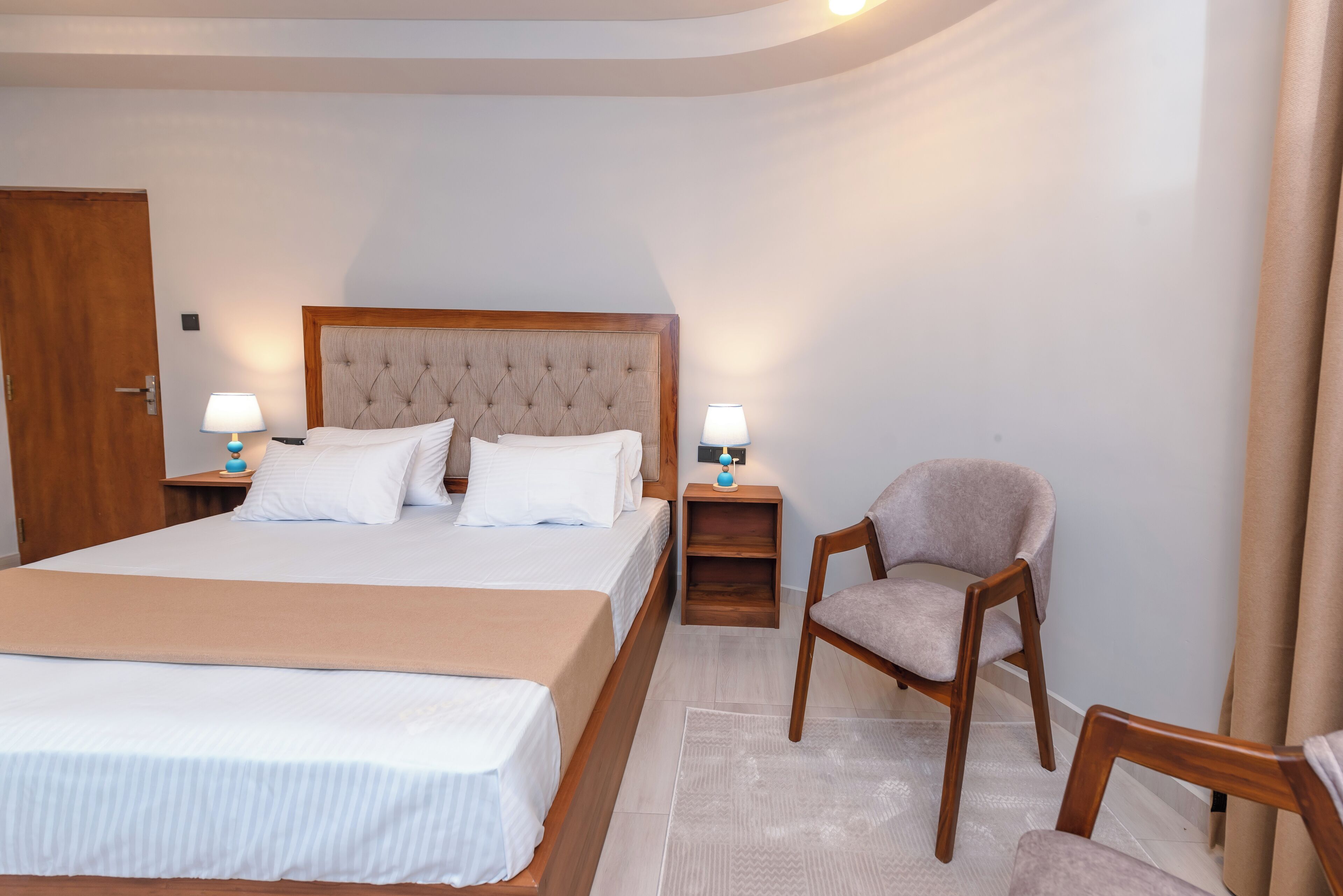 A neatly arranged bedroom with a large bed, two bedside tables with lamps, a wooden chair, and a wooden wardrobe.