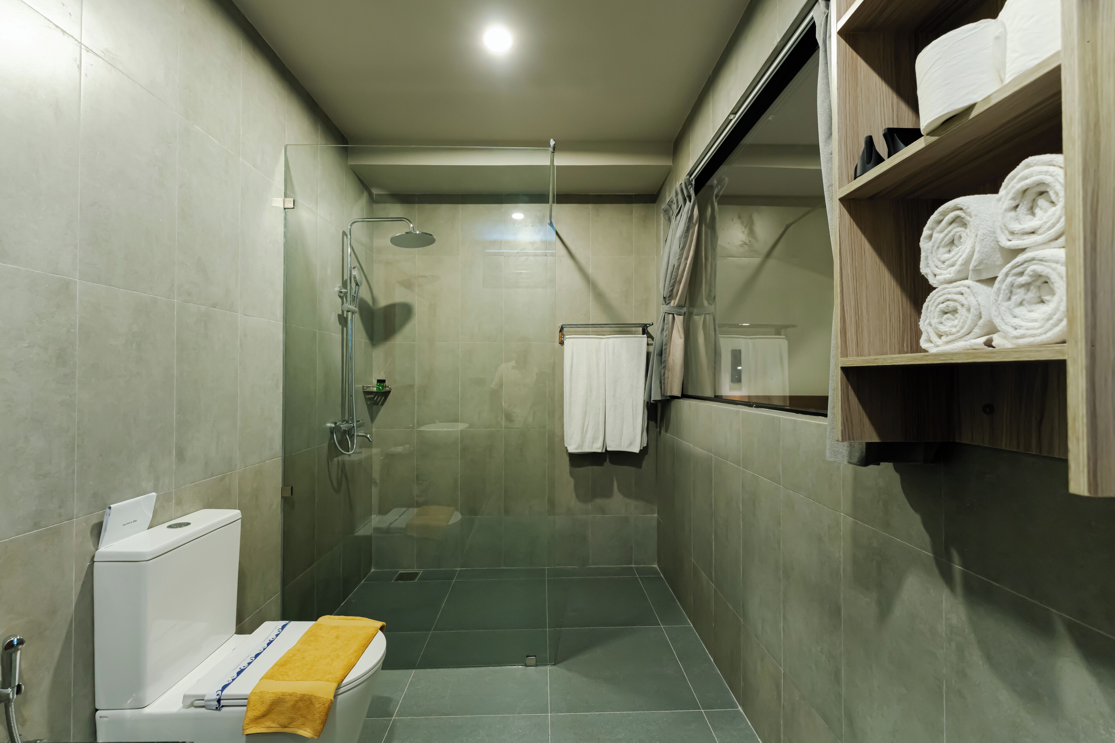 A modern bathroom with a glass-enclosed shower, a toilet with a towel, and a shelf with neatly rolled towels.