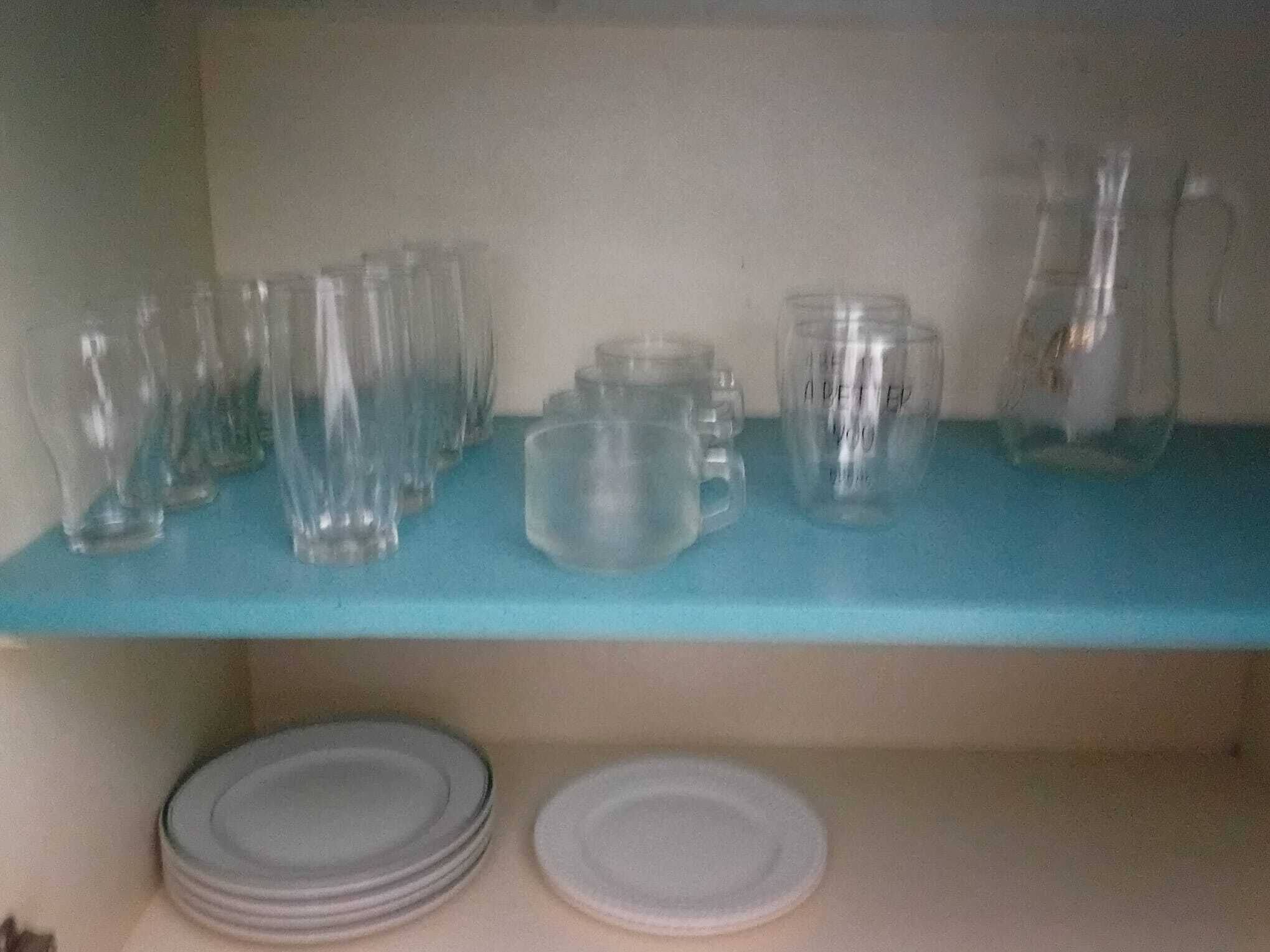 A blue shelf with various glassware including pitchers and mugs, and a stack of plates below.