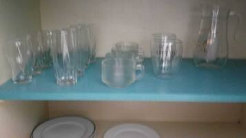 A blue shelf with various glassware including pitchers and mugs, and a stack of plates below.