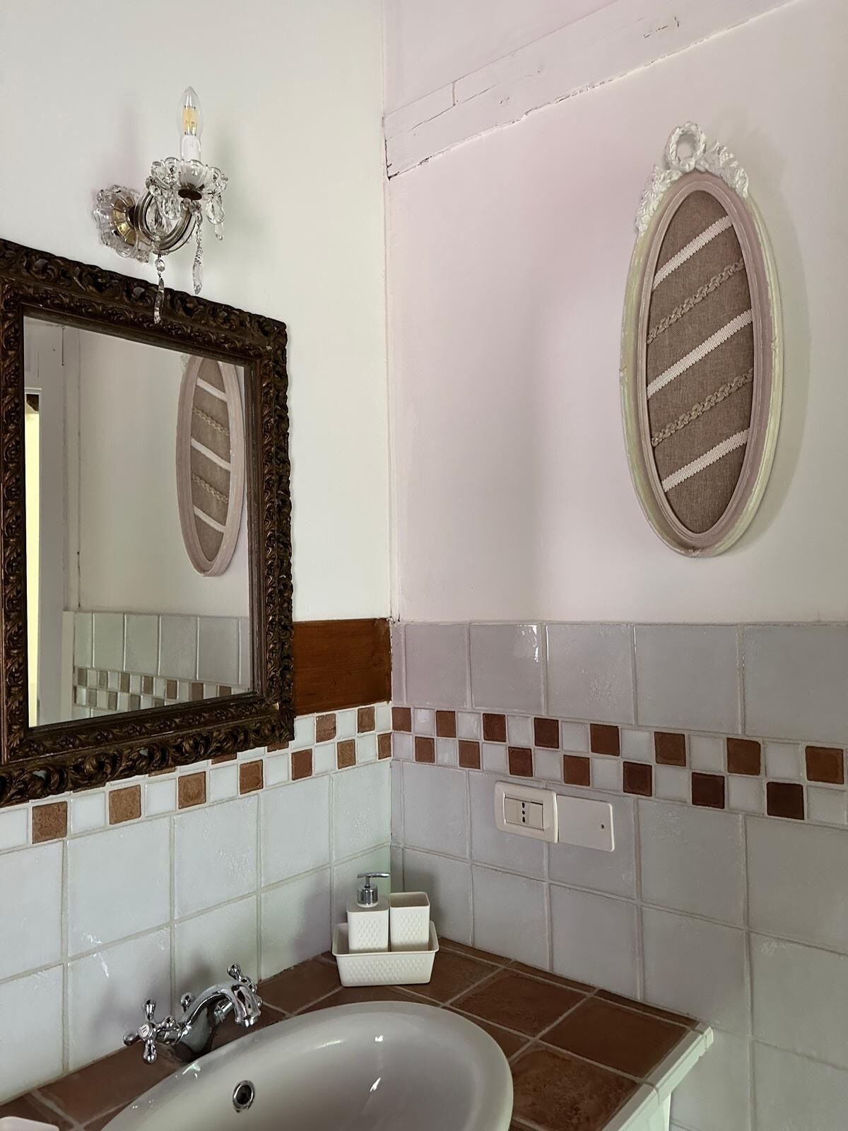 A bathroom with a white sink, a mirror with a brown frame, and a decorative light fixture.