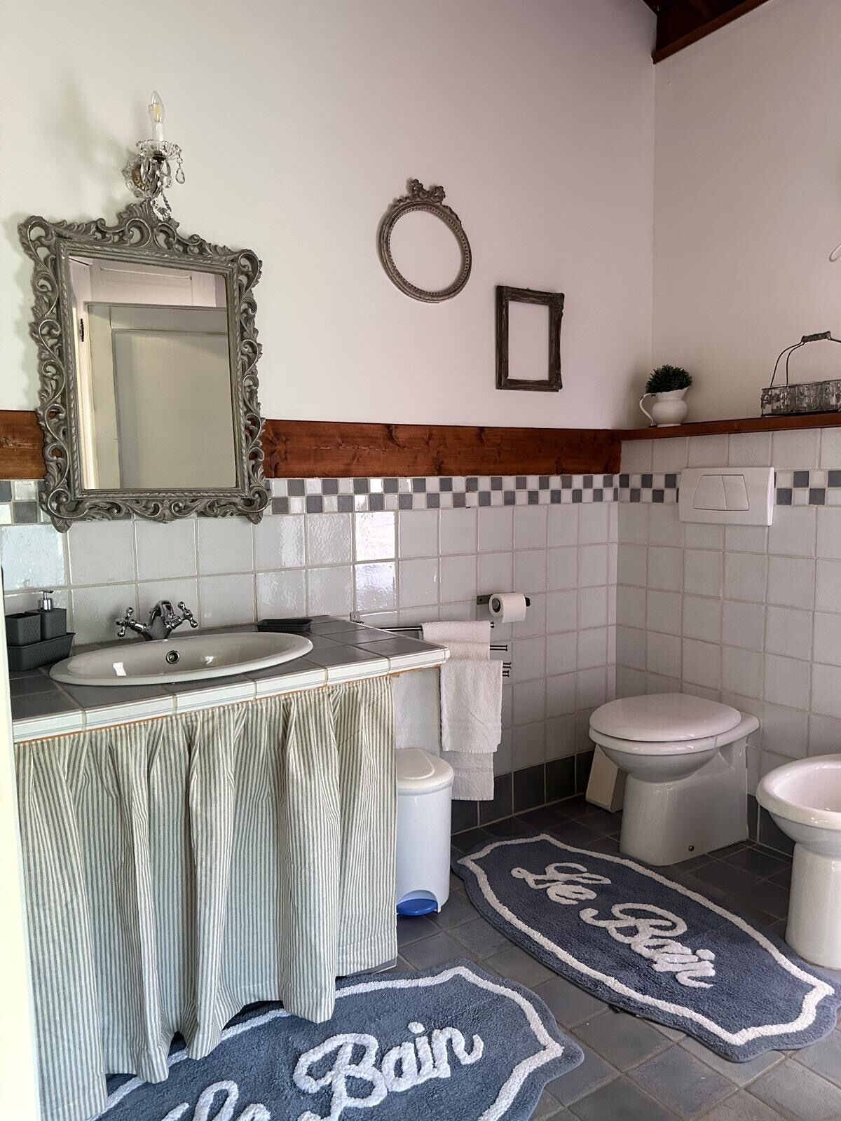 Un baño con lavamanos, espejo, inodoro y bidé. Hay toallas y una planta pequeña en la encimera.