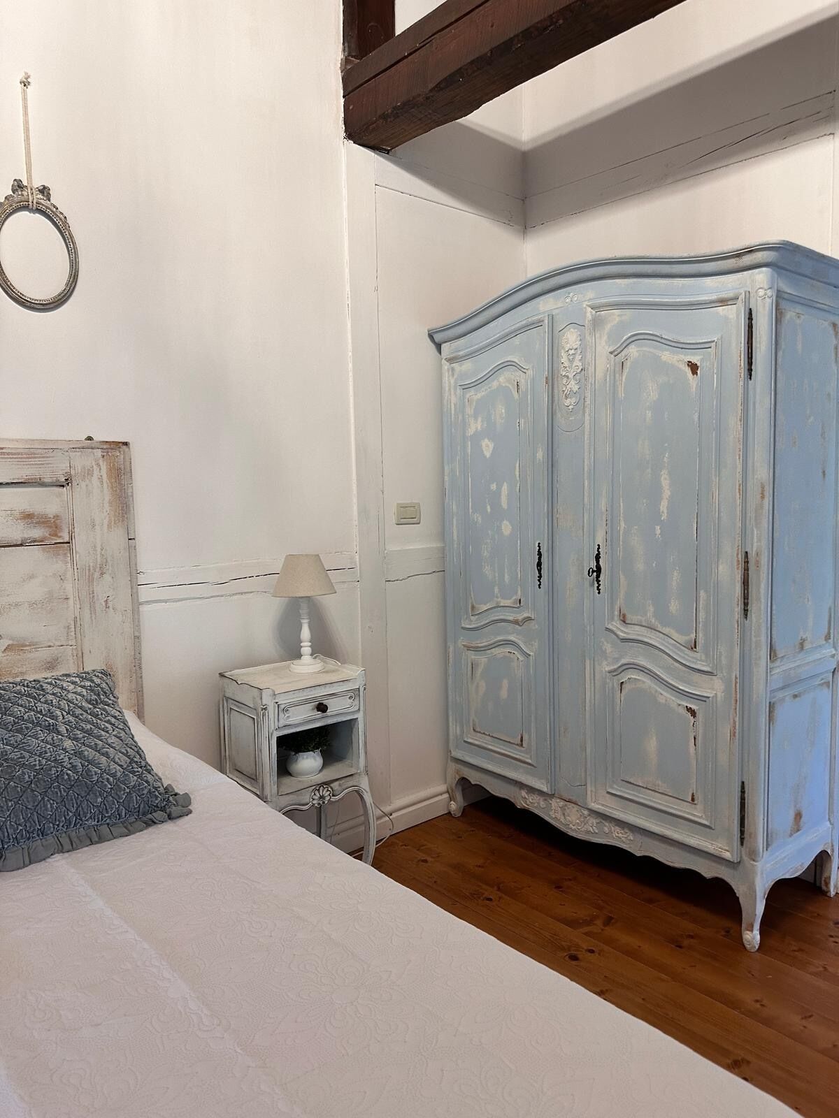 A bedroom with a bed, a nightstand, a dresser, and a ring light on the wall.