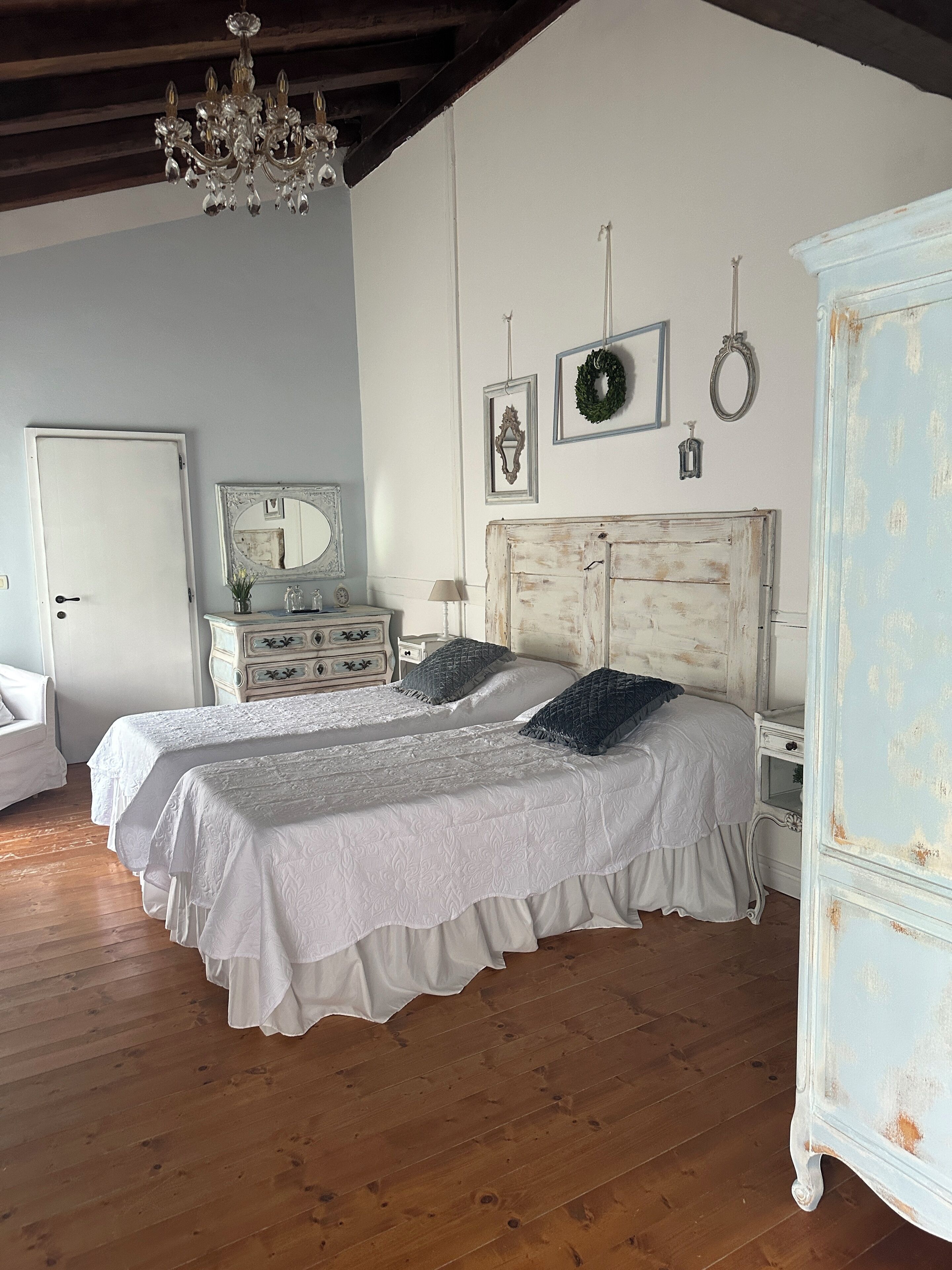 A bedroom with two beds, wooden flooring, a chandelier, and a dresser.