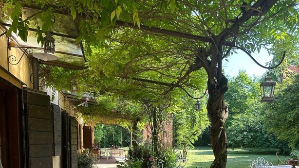 A brick pathway leading to a building with a covered entrance, surrounded by greenery and potted plants. - BednBarchessa (Portogruaro)