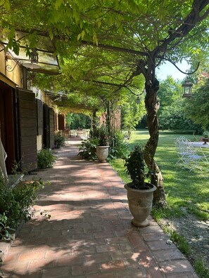 A brick pathway leading to a building with a covered entrance, surrounded by greenery and potted plants. - BednBarchessa (Portogruaro)