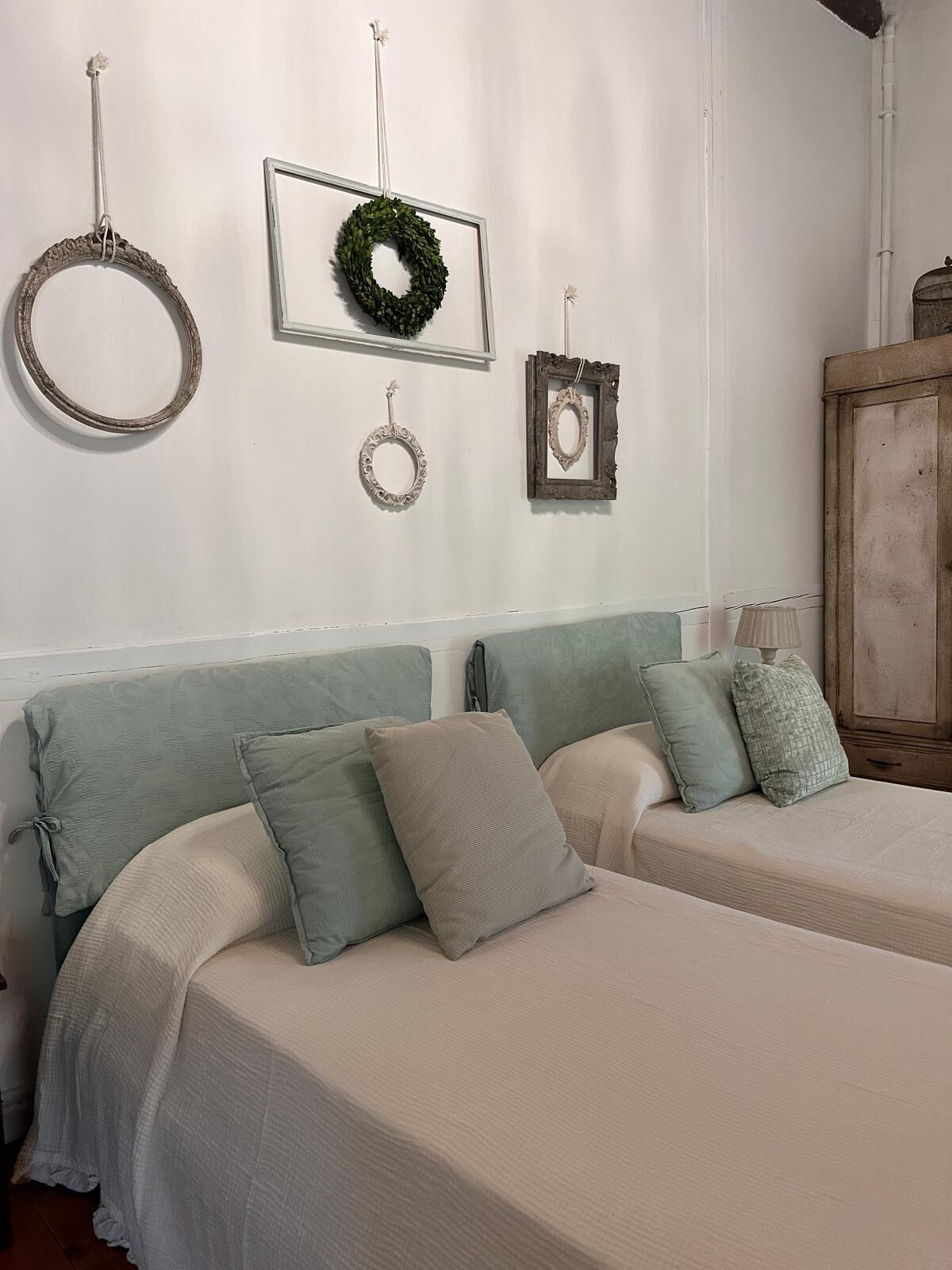 Une chambre avec deux lits, une armoire en bois et des éléments de décoration murale, notamment une guirlande et des miroirs encadrés.