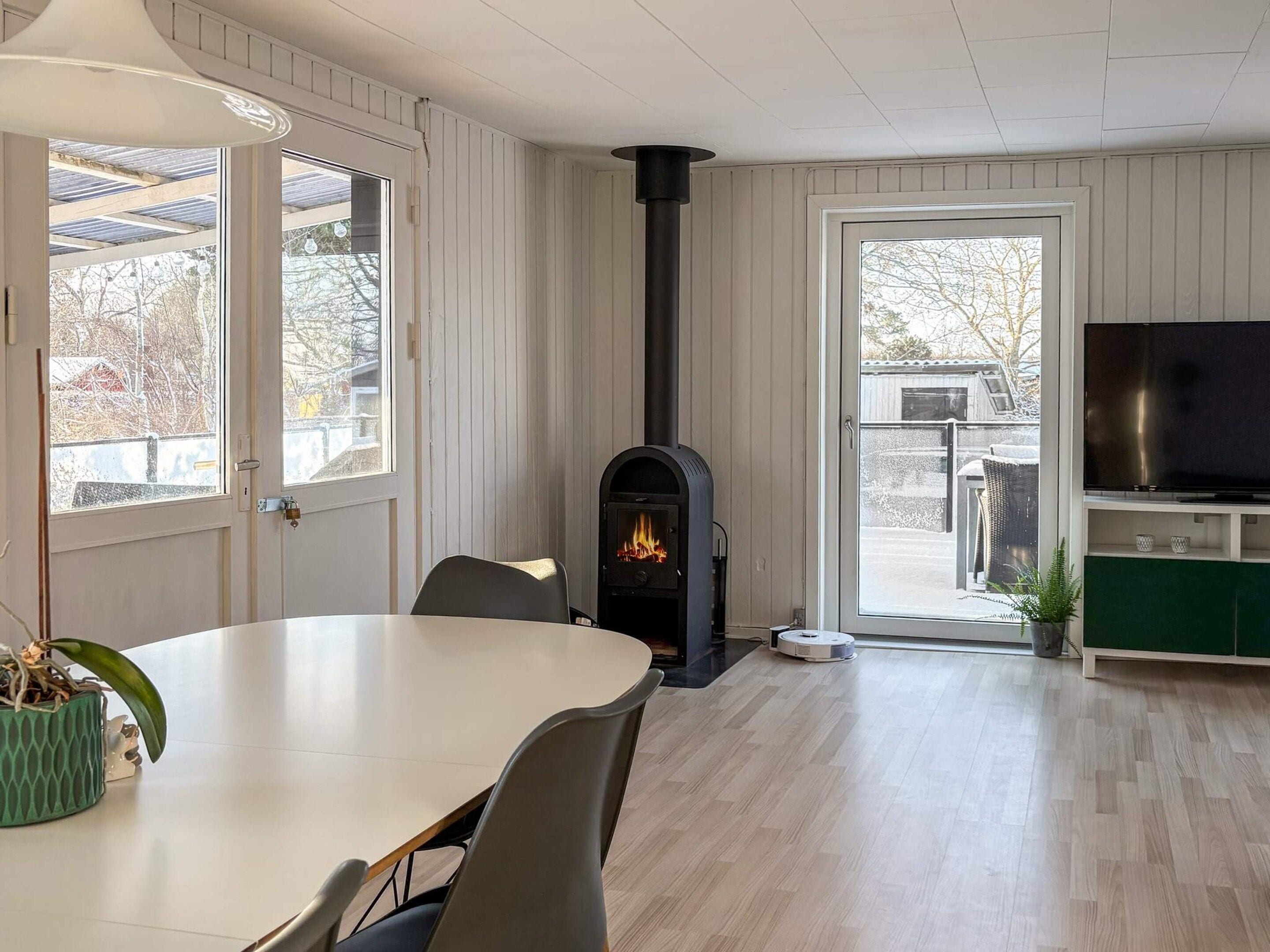 Ein modernes Wohnzimmer mit Kamin, Esstisch, Stühlen, Fernseher und Blick durch eine Glastür.