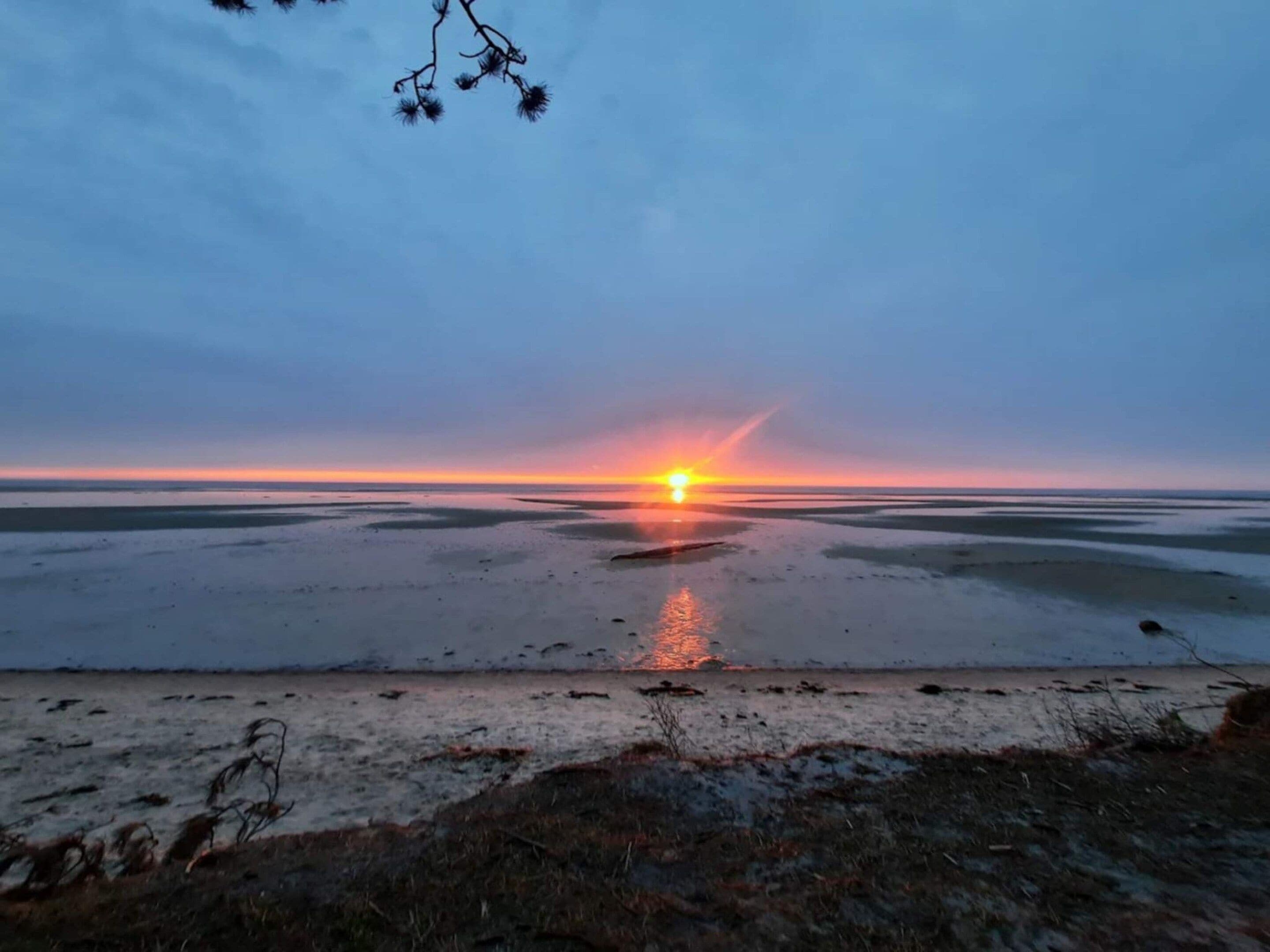 Un coucher de soleil sur un paysage plat, l’eau reflétant le ciel.