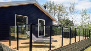 Una casa moderna con terraza de madera, un porche con paredes de vidrio y vistas despejadas del entorno verde.