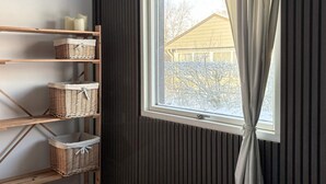 Un dormitorio con una repisa de madera que sostiene cestas, una cama con cubrecama blanco y una ventana con cortinas.