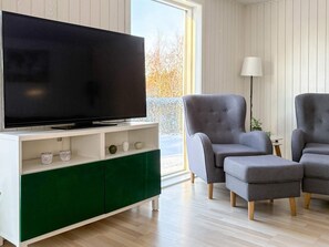 A modern living room with a flat-screen TV on a white and green console, two grey armchairs, and a floor lamp. - 4 Person Holiday Home in Hadsund (Hadsund)